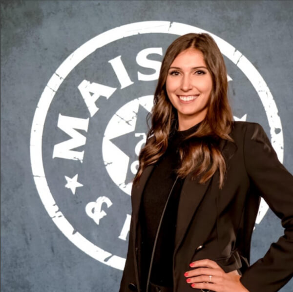 Testimonial – Julia Burkhardt von Meisel & Friends (Keynote-Vortrag) Julia Burkhardt steht lächelnd vor einem grauen Hintergrund mit Logo